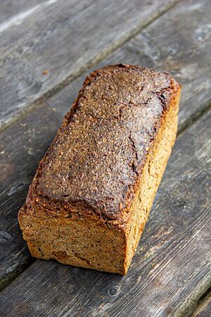 Ein dunkel ausgebackenes Kastenbrot mit glatter, leicht glänzender Kruste liegt auf einem Holztisch.