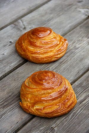 Tourierte Brioche-Brötchen. Zwei tourierte Brioche-Brötchen mit glänzender Oberfläche liegen auf einem rustikalen Holztisch.
