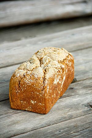 Ein in der Kastenform gebackenes Vollkornbrot liegt auf einem rustikalen Holztisch.