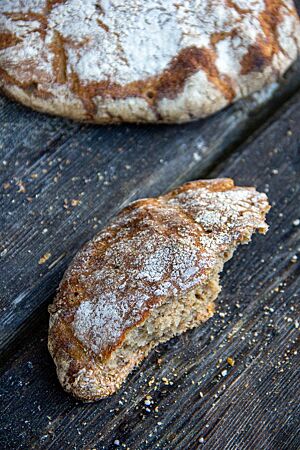 Ein flaches Vinschgauer Brot liegt mit bemehlter Kruste auf einem rustikalen Holztisch.