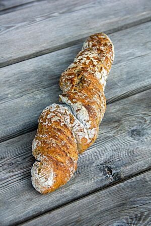 Leinwurzel. Die goldbraun ausgebackene Leinwurzel mit leicht bemehlter Kruste liegt auf einem rustikalen Holztisch.