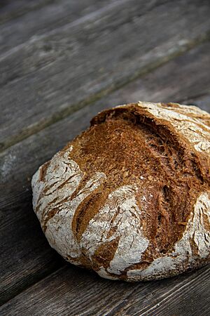 Ein kräftig ausgebackenes, rustikal aufgerissenes Vollkornbrot mit bemehlter Kruste liegt auf einem Holztisch.