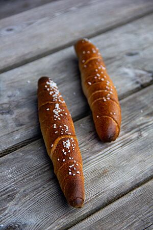 Zwei dunkel ausgebackene, mit grobem Salz bestreute Almstangerl liegen auf einem rustikalen Holztisch.