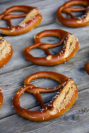 Mehrere Vollkorn-Laugenbrezeln mit rustikal aufgerissenen Brezelbäuchen liegen auf einem Holztisch.