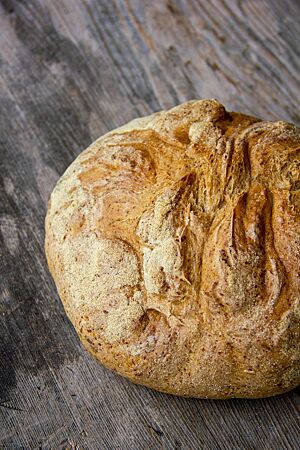 Genetztes Dinkelbrot. Der runde, hellbraun ausgebackene Laib mit rustikalem Ausbund liegt auf einem dunkelgrauen Holztisch.
