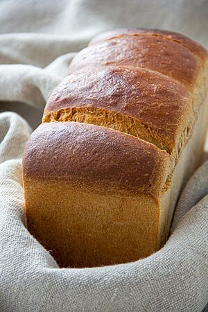Kastenweißbrot mit gekochtem Sauerteig. Ein kräftig ausgebackenes Kastenweißbrot mit unbemehlter Kruste liegt in einem Leinentuch.
