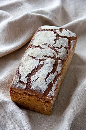 Das kräftig ausgebackene Kastenbrot mit Rissen auf der bemehlten Oberfläche liegt auf einem Leinentuch.