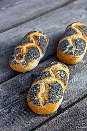 Die geflochtenen, in Mohn gewälzten und mit grobem Salz bestreuten Mohnflesserl liegen auf einem rustikalen Holztisch.