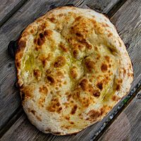 Eine goldbraun ausgebackene Pizza, beträufelt mit Olivenöl und Salz, liegt auf einem rustikalen Holztisch.