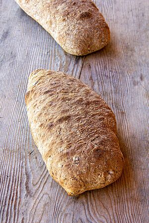 Saaten-Ciabatta. Das kräftig ausgebackene Saaten-Ciabatta mit matter Oberfläche liegt auf einem rustikalen Holztisch.
