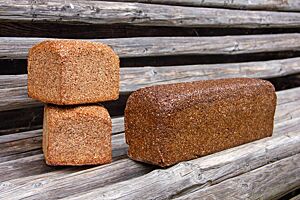 Roggenschrotbrot und Pumpernickel. Zwei kleine Roggenschrotbrote (links) und ein Pumpernickel (rechts) liegen auf einer rustikalen Holzbank.