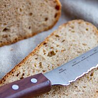 Ein kleines Messer mit dunklem Holzgriff und gezackter Stahlklinge, welche das Profil der Zugspitzregion darstellen soll, liegt auf einer Scheibe Brot.