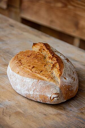 Bayerisches Ruchbrot. Das rustikale, weit aufgerissene Ruchbrot liegt auf einem Holztisch.