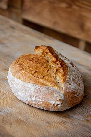 Das rustikale, weit aufgerissene Ruchbrot liegt auf einem Holztisch.