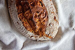 Gemüsebrot. Das kräftig ausgebackene Gemüsebrot mit bemehlter Kruste liegt auf einem Leinentuch.