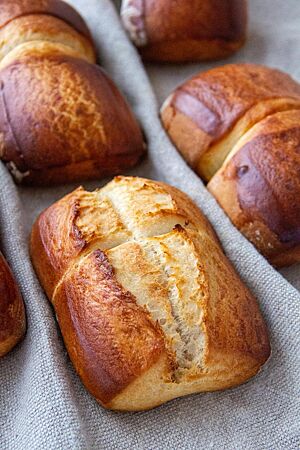 Doppelte Milchbrötchen. Die quadratischen Milchbrötchen wurden paarweise angeschoben gebacken, teilweise mittig eingeschnitten und haben eine glänzende, goldbraun ausgebackene Kruste.