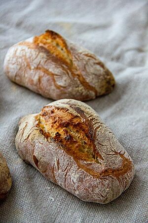 Längliche, mittig aufgerissene Berliner Schlagbrötchen mit krosser, leicht bemehlter Kruste liegen auf einem Leinentuch.