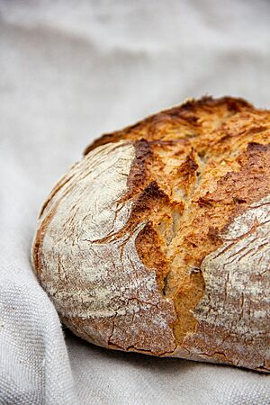 Ein rustikal aufgerissenes Brot mit leicht bemehlter Kruste liegt auf einem Leinentuch.
