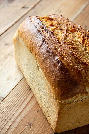 Ein goldbraun ausgebackenes Toastbrot mit glänzender Kruste liegt auf einem Holztisch.