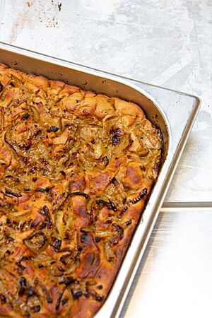 Stavanger Roggenfocaccia. Die goldbraun ausgebackene Roggenfocaccia liegt in einem tiefen Blech und ist mit karamellisierten Zwiebeln belegt.