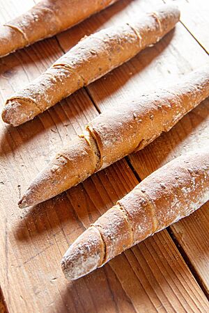 Kornstangen – Rezeptvariante. Knusprige Stangen mit eingearbeiteten Saaten liegen leicht bemehlt auf einem Holztisch.