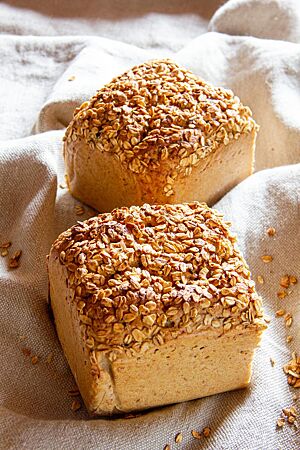 Roggenmischbrot mit Hafer. Zwei goldgelb ausgebackene Roggenmischbrote mit Haferflocken auf der Kruste liegen auf einem Leinentuch im Sonnenschein.
