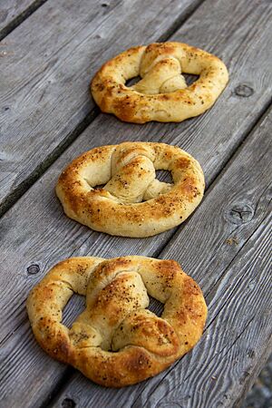 Drei dicke hellbraune Brezeln mit gemahlenem schwarzem Pfeffer auf der Kruste liegen auf einem grauen Holztisch.