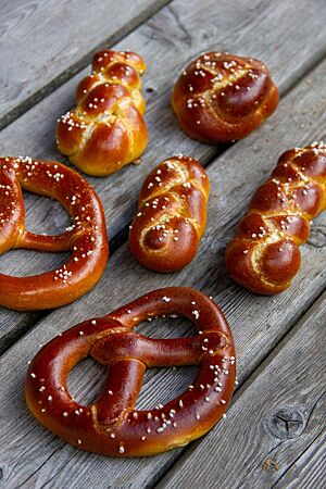 Dreikornbrezel. Zwei Brezeln, ein Knoten und drei kleine Zöpfe sind auf ihrer dunkelbraunen Kruste mit weißen Salzkörnern bestreut.