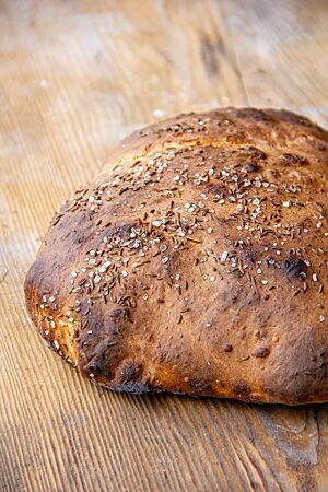 Petras Eingenetztes. Das kräftig ausgebackene Dinkelbrot mit Salz und Kümmel auf der Kruste liegt auf einem rustikalen Holztisch.