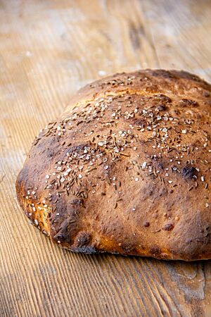 Das kräftig ausgebackene Dinkelbrot mit Salz und Kümmel auf der Kruste liegt auf einem rustikalen Holztisch.