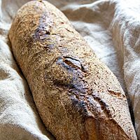 Ein längliches Brot mit bemehlter Kruste liegt kräftig ausgebacken in einem Leinentuch.