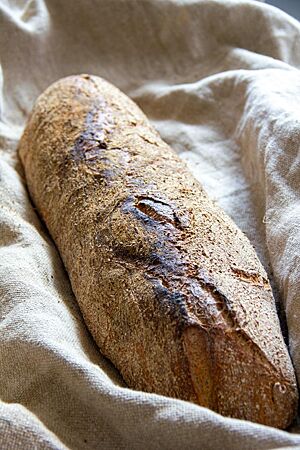 Ein längliches Brot mit bemehlter Kruste liegt kräftig ausgebacken in einem Leinentuch.