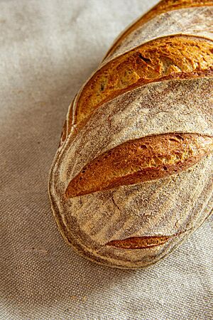 Mill Loaf. Das kräftig ausgebackene, rustikal aufgerissene Weizenbrot mit leicht bemehlter Kruste liegt auf einem Leinentuch.
