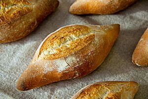 Fränkischer Kipf. Goldbraun ausgebackene Weizenbrötchen liegen rustikal aufgerissen auf einem Leinentuch.