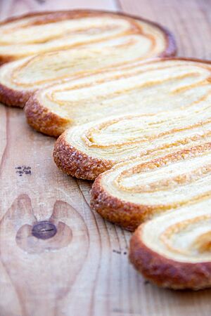 Eine Reihe angeschoben gebackener Schweinsohren liegt auf einem hellen Holztisch.