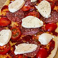 Auf dem dünn ausgezogenen Pizzateigling befinden sich Tomaten, Salami und Mozzarella.