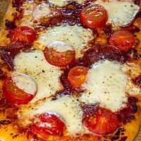 Die ausgebackene Pizza ist mit Tomaten, Salami und Mozzarella belegt.