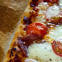 Geschmolzener Mozzarella, Tomaten und Salami liegen auf der knusprig ausgebacken Pizza.