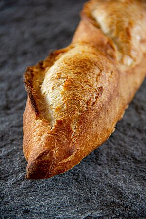 Das goldbraun ausgebackene, rustikal aufgerissene Baguette liegt auf der Arbeitsfläche.