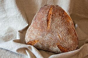 Das goldbraun ausgebackene, dreieckige Roggen-Dinkel-Brot mit Grieß auf der Oberfläche hat drei kleine Einschnitte an jeder Spitze des Dreiecks.