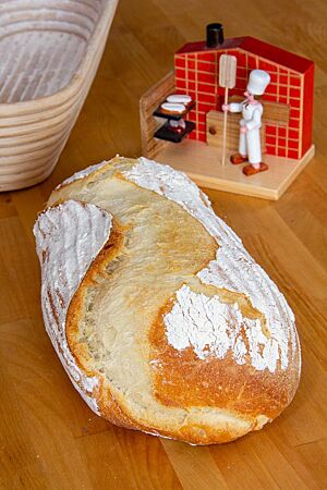 Das mit Camembert gefüllte Weißbrot liegt mit rustikal aufgerissener Kruste auf einem Holztisch.