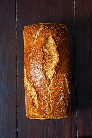 Der glänzende, goldbraun ausgebackene Brotlaib vom Sejerlänner Riewekooche liegt auf einem dunklen Holztisch.