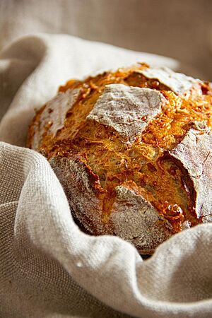 Das goldbraun ausgebackene, rustikal aufgerissene Harzer Kümmelbrot mit leicht bemehlter Kruste liegt in einem Leinentuch.