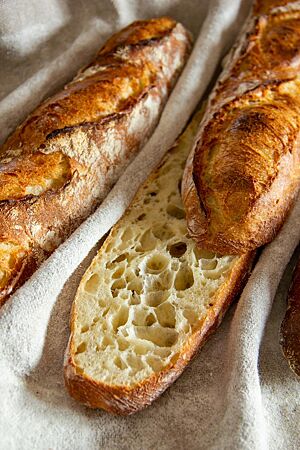 Baguette mit T 65: grobporige, unregelmäßige Krume. Das angeschnittene Baguette mit splittriger Kruste hat eine grobporige und unregelmäßige Krume.