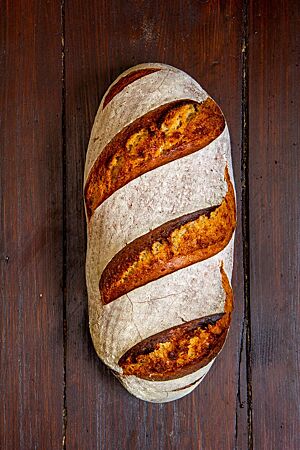 Ein kräftig ausgebackenes, rustikal aufgerissenes Roggenmischbrot mit bemehlter Kruste liegt auf einem Holztisch.