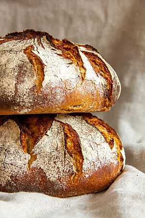 Rustikales Bauernbrot. Zwei rustikale Bauernbrote liegen aufeinandergestapelt auf einem Leinentuch.