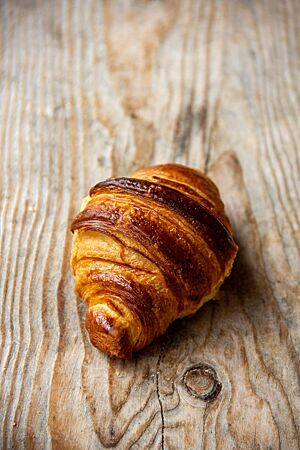 Ein goldbraun glänzendes Croissant mit blättrigen Schichten liegt auf einem Holzbrett.