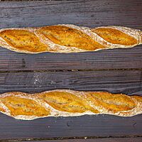 Zwei kleine, dünne Brotstangen mit langen, spitz geformten Enden liegen auf einem Holztisch.