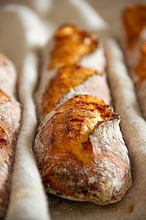 Das kräftig ausgebackene, rustikal aufgerissene Kamutbaguette mit bemehlter Kruste liegt in einem Leinentuch.