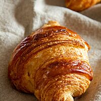 Ein goldbraun glänzendes Croissant mit sichtbaren Schichten liegt auf einem Leinentuch.